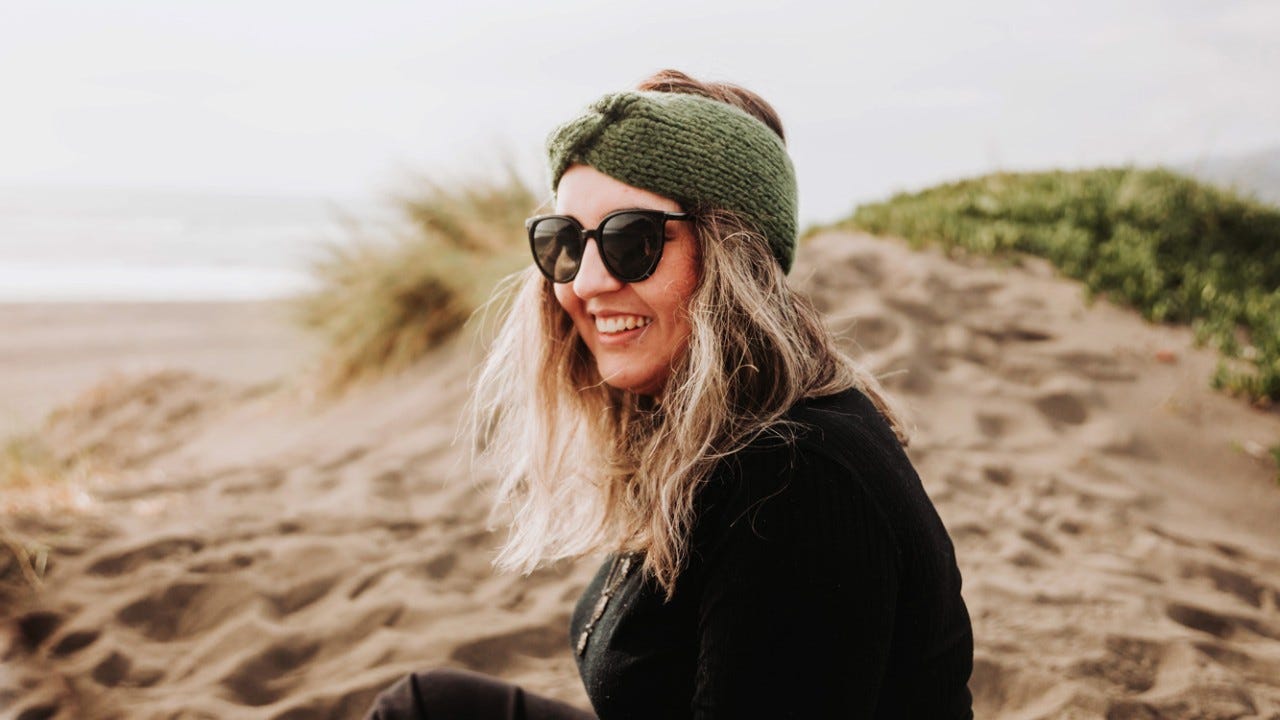 1415069498 Smiling blonde plus size woman dressed in black, wearing a headband, sunglasses and sitting on the beach. Overcoming depression