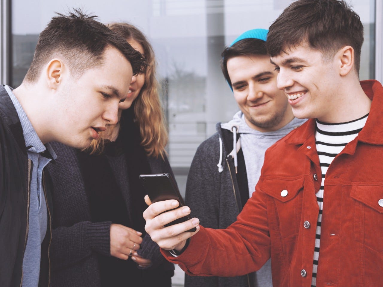 young man showing something funny on his smartphone to a group of teenage friends, focus on hand holding mobile phone, matte filter