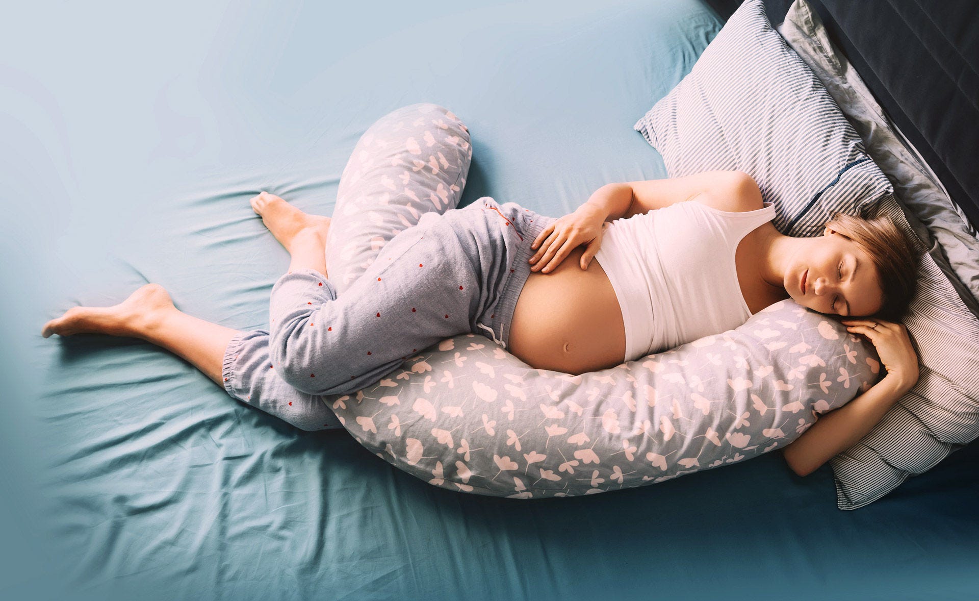 Schwangere Frau schläft in Seitenlage mit Stillkissen.