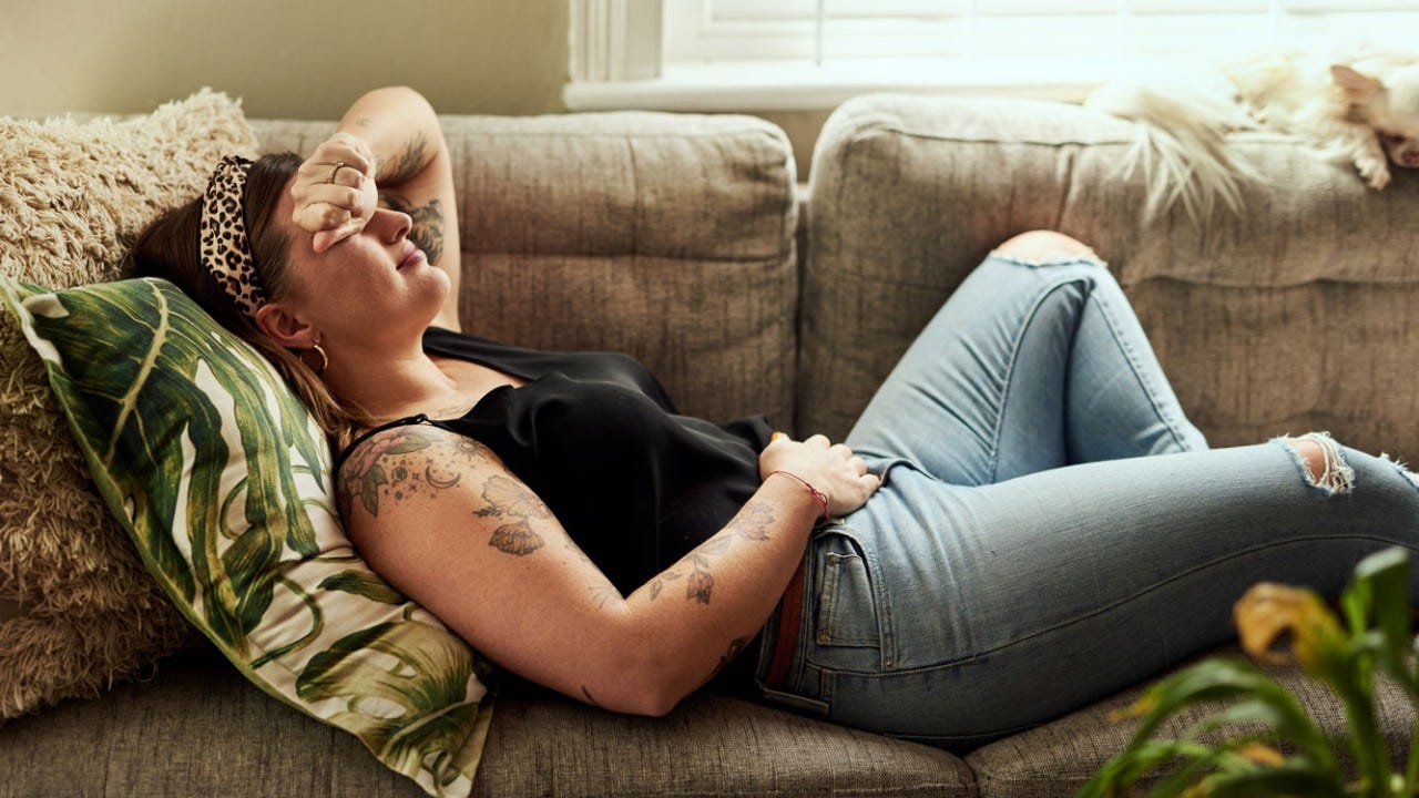 Shot of a young woman suffering from stomach cramps on the sofa at home