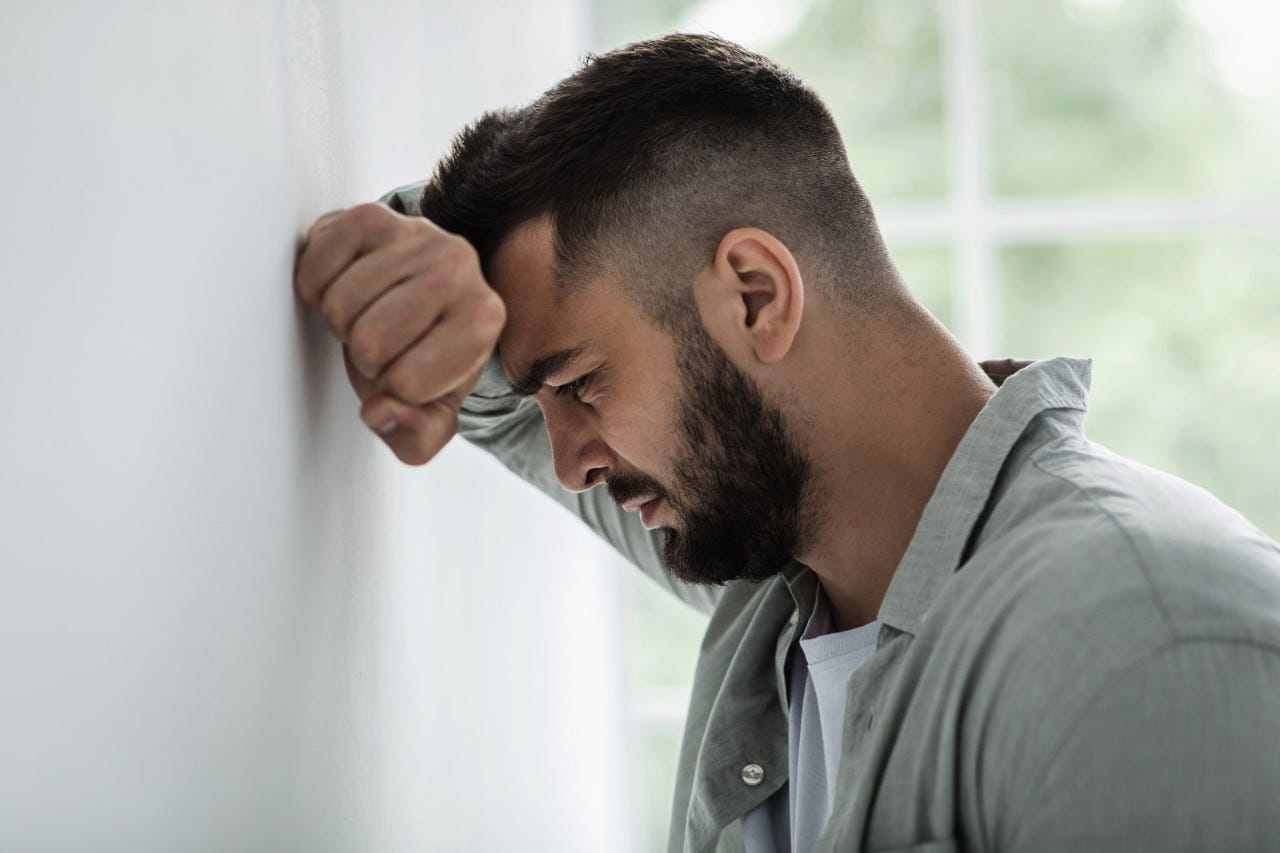 1329038059 Emotional stress and unhappy, despair, grief and negative emotions, anxiety and agoraphobia. Sad millennial attractive bearded guy resting hand on gray wall and crying, suffer from pain and problems